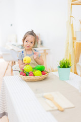 Beautiful little girl with fruits  in basket on kitchen table at house