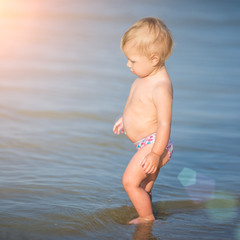 Baby playing on the sandy beach and in sea water. Cute little kid with toys on sand tropical beach. Ocean coast.