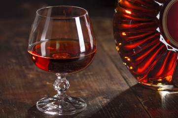 Glass of cognac and bottle of cognac on vintage wooden background. Low depth of field. 