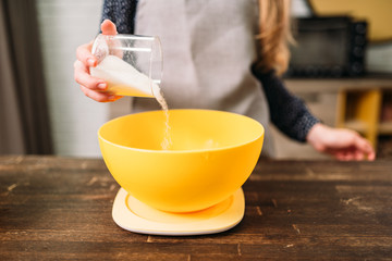 Female hands adds sugar into a bowl with dough
