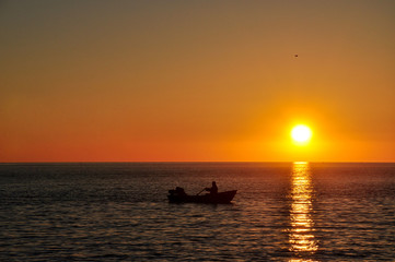The boat with the fishermen in the sea at sunset.
