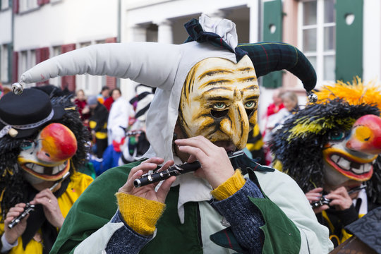 Basel carnival. Nadelberg, Basel, Switzerland - March 7, 2017. Closeup of a single participant with a clown mask and a green and white costume playing piccolo.