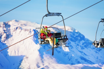 Fototapeta na wymiar Two skiers lifting on lift against snowy mountains