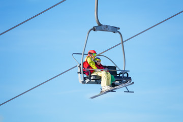 Two skiers lifting on chairlift against blue sky
