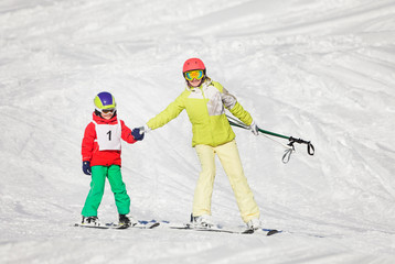 Active mother teaching son skiing holding hands