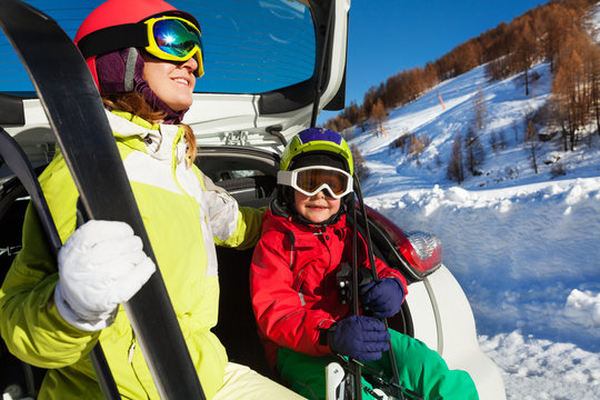 Woman and son in skiing suits sitting on car trunk