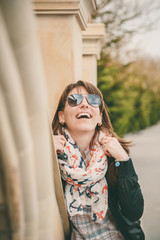 Young smiling happy girl in sunglasses, black jacket and anchors scarf outdoors. Portrait of beautiful smiling woman. Lifestyle concept.