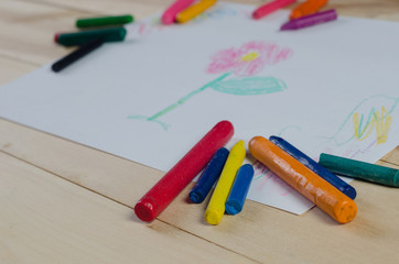 Wax crayons on white sheet, wooden background