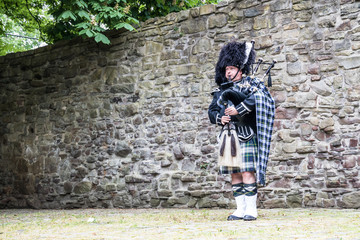 Traditioneller schottischer Dudelsackspieler vor historischer Mauer