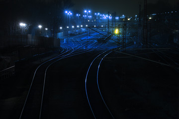railway tracks at night lead shiny and curving to a cargo freight station, copy space in the dark background