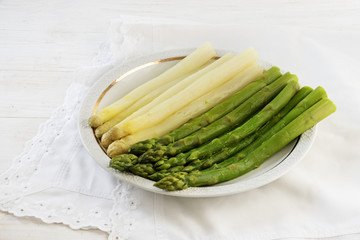 cooked asparagus, green and white on a plate, white table with napkin, copy space