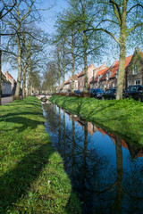 Fototapeta na wymiar Walking along the small canal in old Dutch village, sunny Sunday morning, spring season.