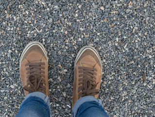 Legs of a girl in brown sneakers and jeans on a gravel background
