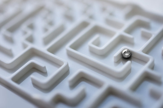 White labyrinth and metal ball, complex problem solving concept.