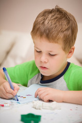 Portrait of cute kid boy drawing at the table at home. Child making craft. Education, creativity and early learning.