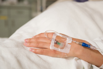 Close up hand of young patient with intravenous catheter for injection plug in hand during lying in the hospital bed. - 145384210