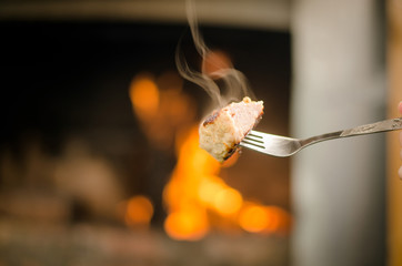 Smoky barbeque pork meat on the fork. Meat on the coals with blurred bonfire background.