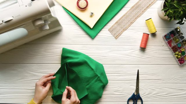 Woman hands cutting fabric cloth with scissors on white designer desk. Top view. Green fabric cloth. Designer, tailor. Slow motion