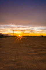 Rays of sun on an empty dirt road with telephone poles and mountains in the background.