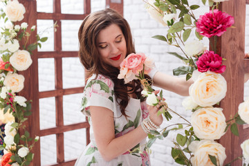 Beautiful young brunette woman with long curly hair is smelling the flowers.