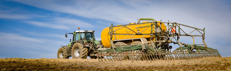 Tractor with yellow vacuum manure spreader on a field, wide format