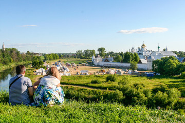Man and woman look at the Intercession Monastery from the bank of the river Kamenka, Russia, Suzdal - obrazy, fototapety, plakaty