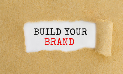 Text Build Your Brand appearing behind ripped brown paper.