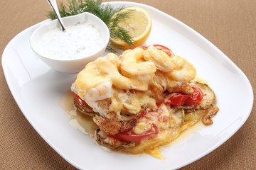 Baked vegetables and shrimps with cheese served with lemon and white sauce
