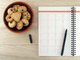 notebook with pen and biscuit cookies on wooden table floor, diary calendar for planning, closeup top view