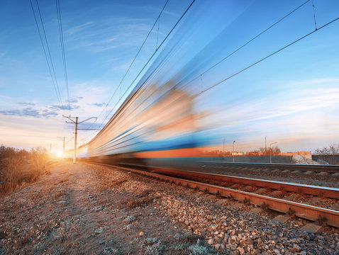 Fototapeta High speed train in motion on railroad track at sunset. Blurred commuter train. Railway station against colorful blue sky. Railroad travel, railway tourism. Rural industrial landscape in twilight