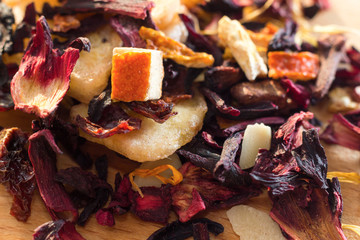 Pile of fruit tea with petals and dry fruit .The composition of the heap of tea leaves and dried hibiscus flower located on a wooden Board. Tea with natural ingredients closeup. Macro photo of tea. © rtvistlive