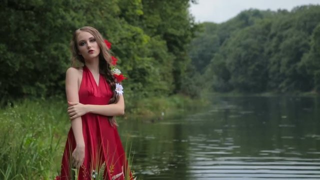 2 shots. Unusual and mysterious girl with creative make-up and elegant hairstyle with flowers in ethnic red dress walking in water. Fashion, mysterious and nature concept