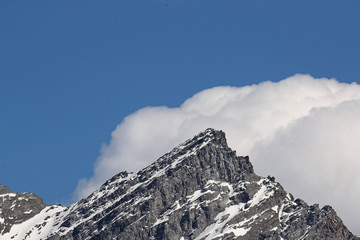 Mountain peak in the clouds with snow against blue skies 