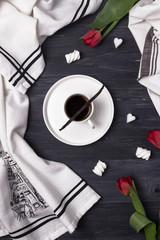 Black coffee in a white cup, vanilla bean, marshmallow and red tulips on a dark background. Top view