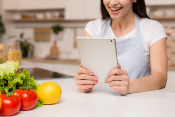 Young Woman in kitchen with tablet computer and looking recipes, smiling. Food blogger concept