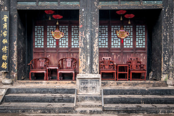 façade d'un vieux bâtiment chinois avec des fauteuils en bois rouges sous les porches 