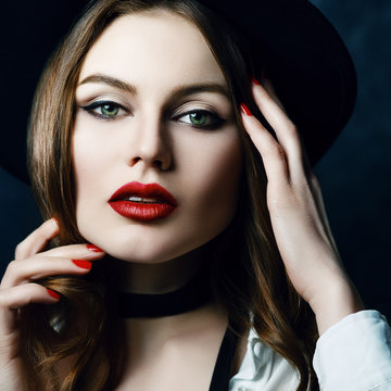 Close up indoor, studio portrait of young attractive woman with beautiful classic makeup, red lips posing on dark background. Model looking at camera. Female beauty, fashion concept