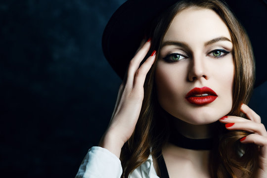 Close up studio portrait of young attractive woman with beautiful makeup, red lips posing on dark background. Model looking at camera. Female beauty, fashion concept. Copy, empty space for text.
