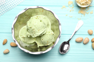 Tasty pistachio ice cream in bowl and nuts on wooden table