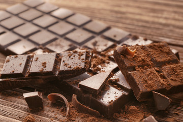 Broken chocolate pieces and cocoa powder on wooden background