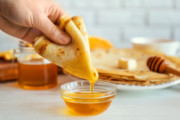 Female hand dunking delicious pancake into bowl with honey