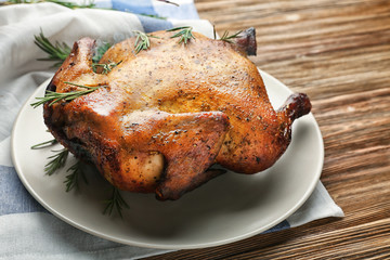 Plate with roasted beer can chicken on wooden background