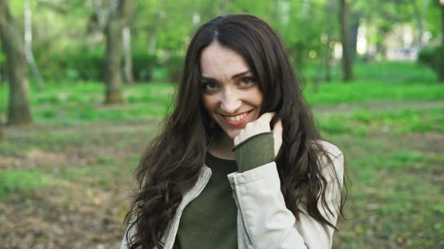 Cheerful brunette girl smiling and laughing looking at the camera and after that walking away from camera in the park