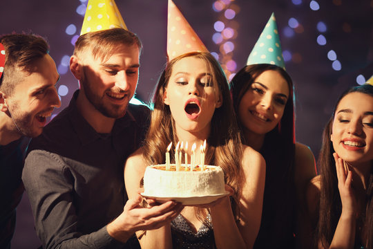 Young Woman Blowing Out Candles On Birthday Cake At Party