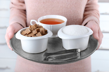Woman holding metal tray with sugar bowls and cup of black tea
