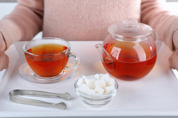 Woman holding wooden tray with sugar bowl, teapot and cup of black tea