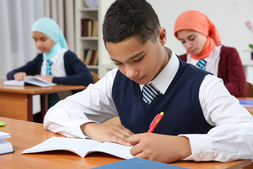 Cute boy sitting at desk in school class