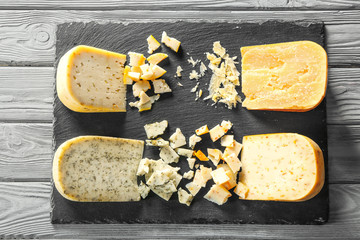 Slate plate with four sorts of cheese on wooden background