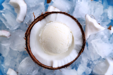 Half of coconut with fresh ice cream ball cooling on icy cubes in blue bowl