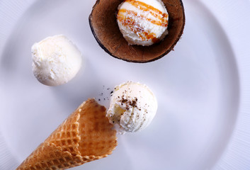 Plate with composition of ice cream balls in waffle cone and coconut shell, closeup